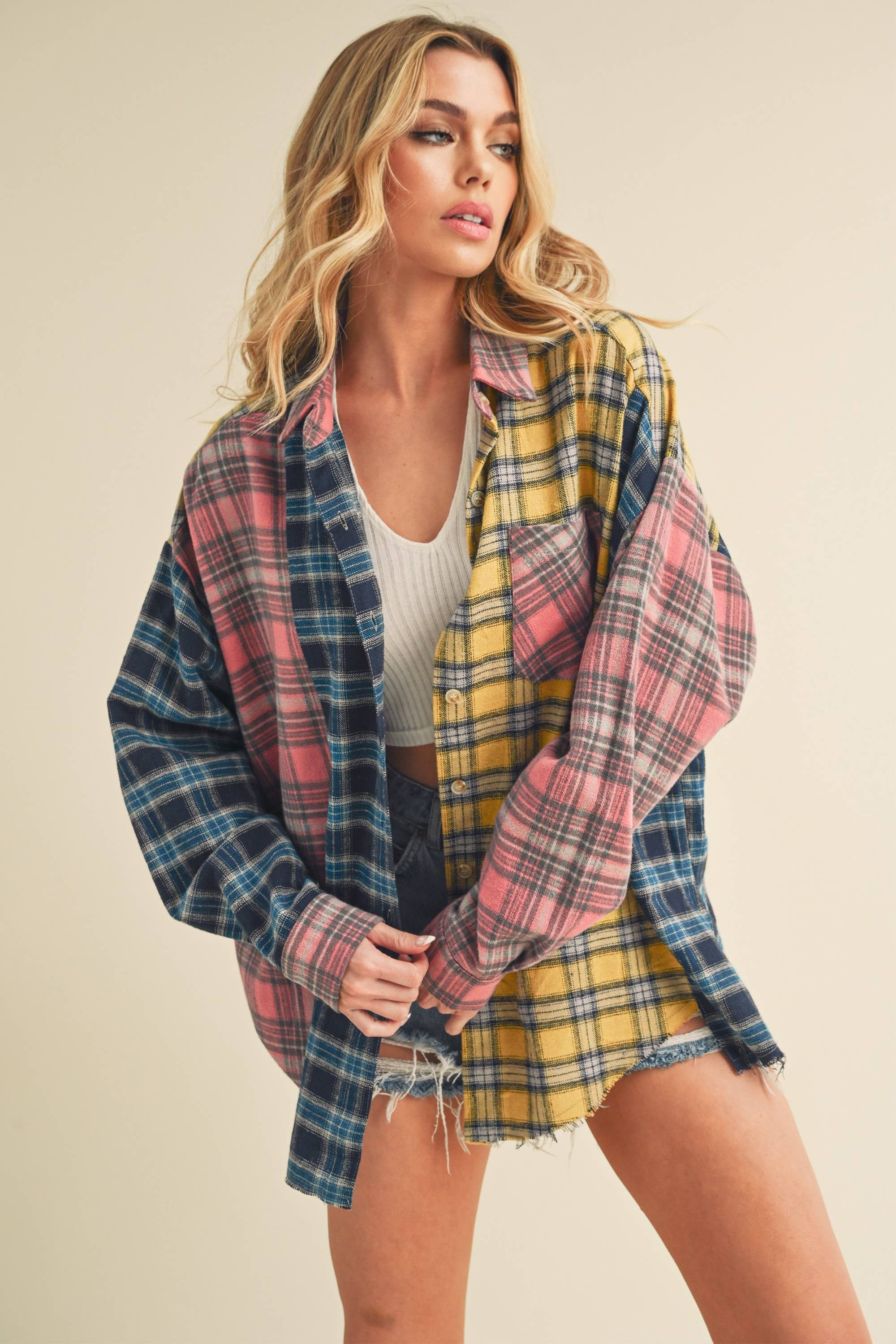 Woman wearing an oversized plaid colorblock flannel shirt in pink, yellow, and navy tones with raw hems.