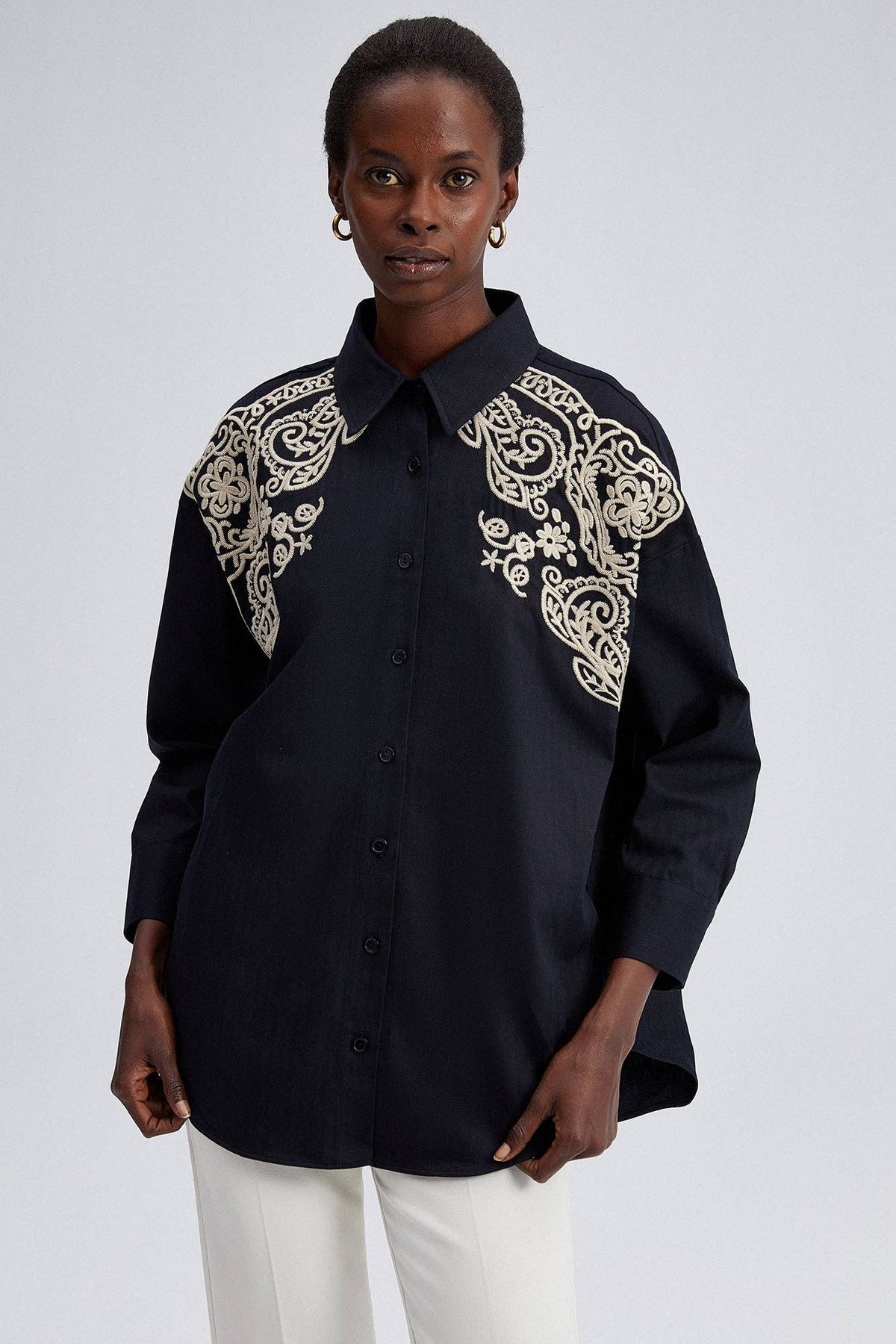 Model wearing black oversized shirt with cream embroidery on shoulders and front yoke.
