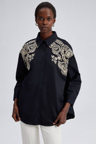 Model wearing black oversized shirt with cream embroidery on shoulders and front yoke.