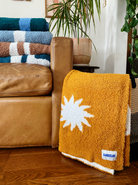 Cozy plush throw blanket in buckhorn brown with a white sunburst pattern, draped over a leather couch in a stylish and inviting living room.