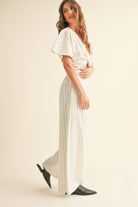 Woman wearing a two-piece striped set with a twist-front crop top and wide-leg pants in cream and tan color options.