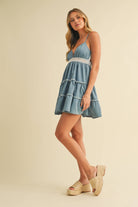 Woman wearing a sleeveless tiered mini dress with crochet waist and plunging neckline in a soft denim blue tone.