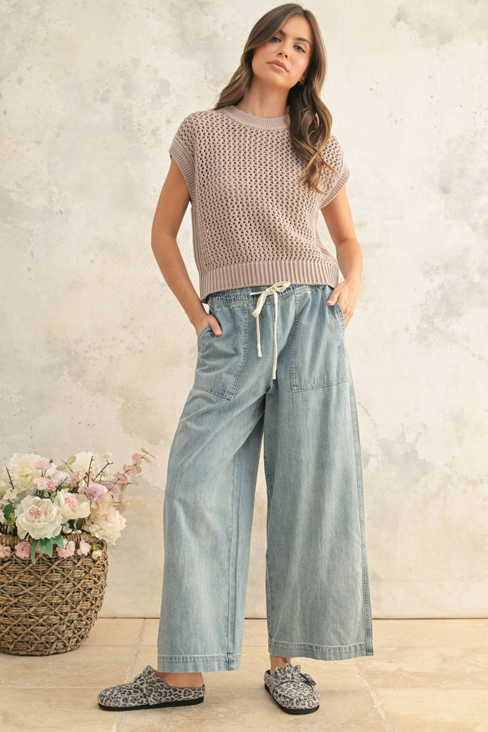 Woman wearing light wash wide-leg denim pants with elastic drawstring waist and front patch pockets.