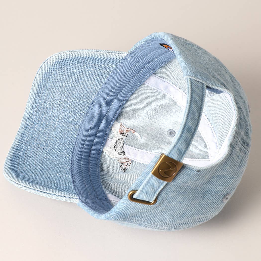 Light blue denim cap with embroidered design on a beige background