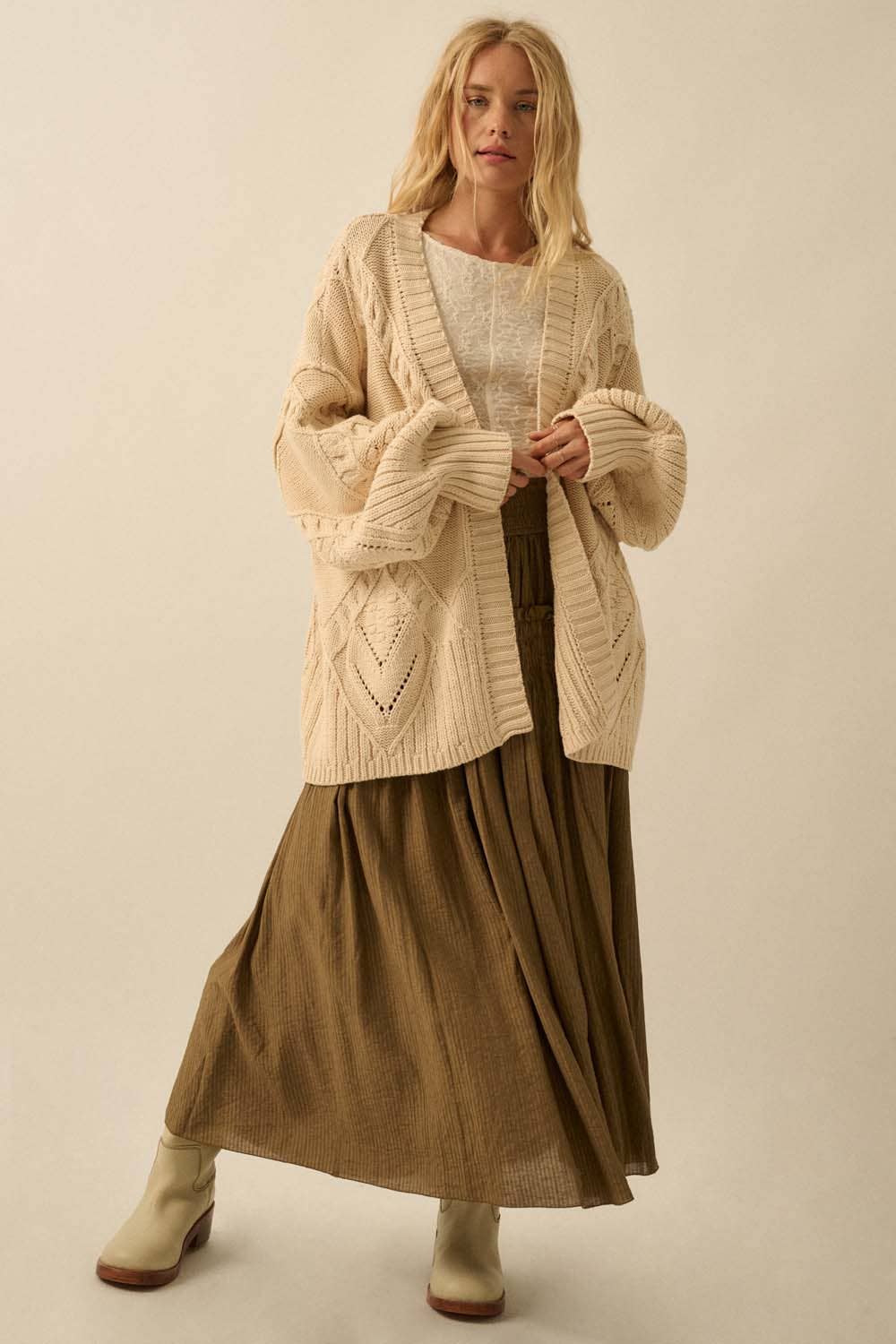 Woman wearing a beige cardigan over a white top and brown skirt on a beige background