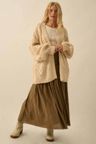 Woman wearing a beige cardigan over a white top and brown skirt on a beige background