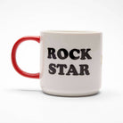 White ceramic mug with a red handle featuring a cool character playing a guitar, surrounded by yellow stars, with "Rock Star" printed on the back.