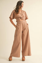 Woman wearing a two-piece striped set with a twist-front crop top and wide-leg pants in cream and tan color options.