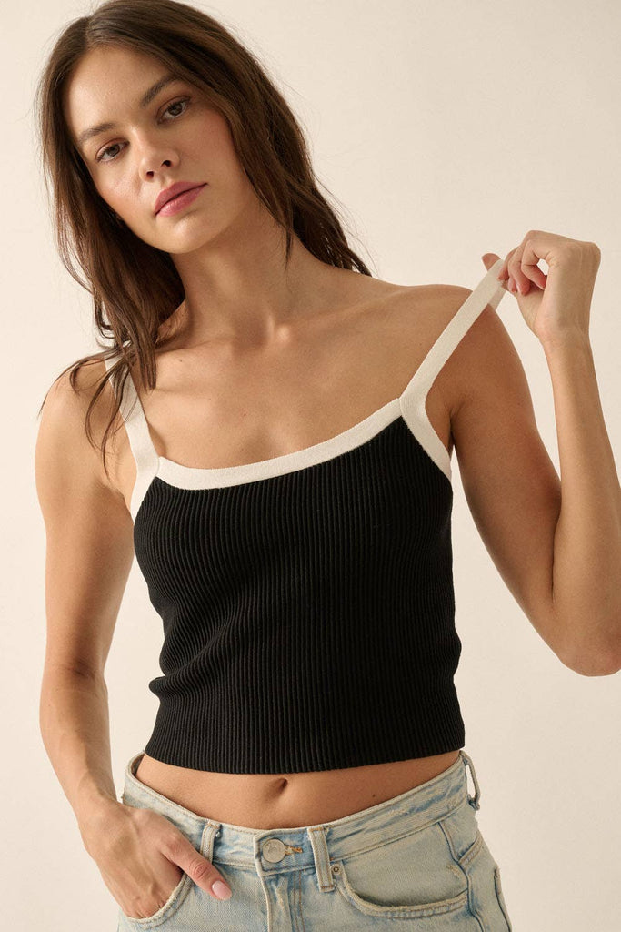 Black ribbed knit tank top with white trim on the straps and neckline, styled with light-wash denim jeans.