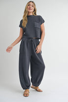 Woman wearing pleated bottom knitted pants in relaxed fit with drawstring waist and ankle detail.