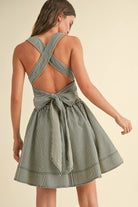 Woman wearing a sleeveless striped mini dress with criss-cross back straps and a large bow tie at the waist.
