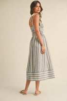 Woman wearing a blue and cream striped midi dress with smocked bodice and tie shoulder straps.