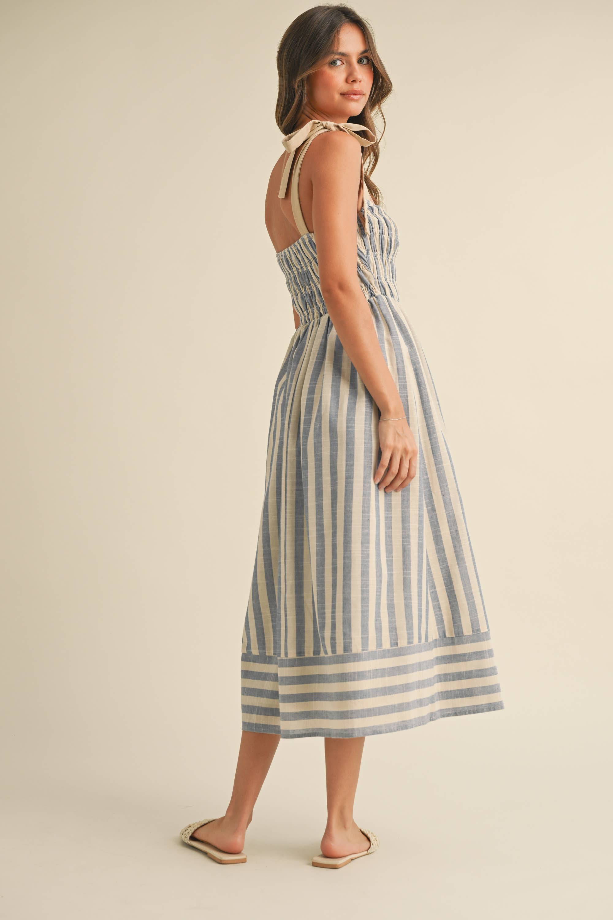 Woman wearing a blue and cream striped midi dress with smocked bodice and tie shoulder straps.