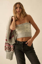 Woman wearing a strapless knitted top and dark jeans, holding a patterned sweater.