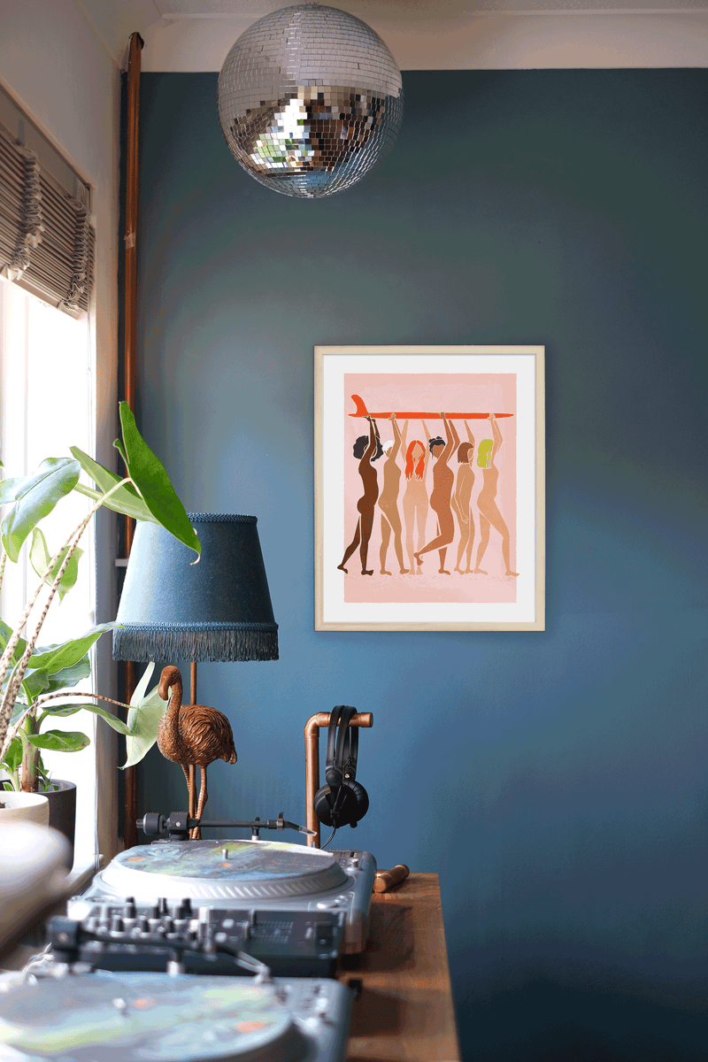 Helping Hands Print featuring diverse women standing together and holding a surfboard, framed in a wooden frame.