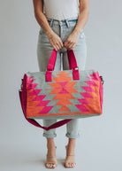 Vibrant weekender bag with orange and hot pink geometric design, held by woman in light wash jeans and white tank top