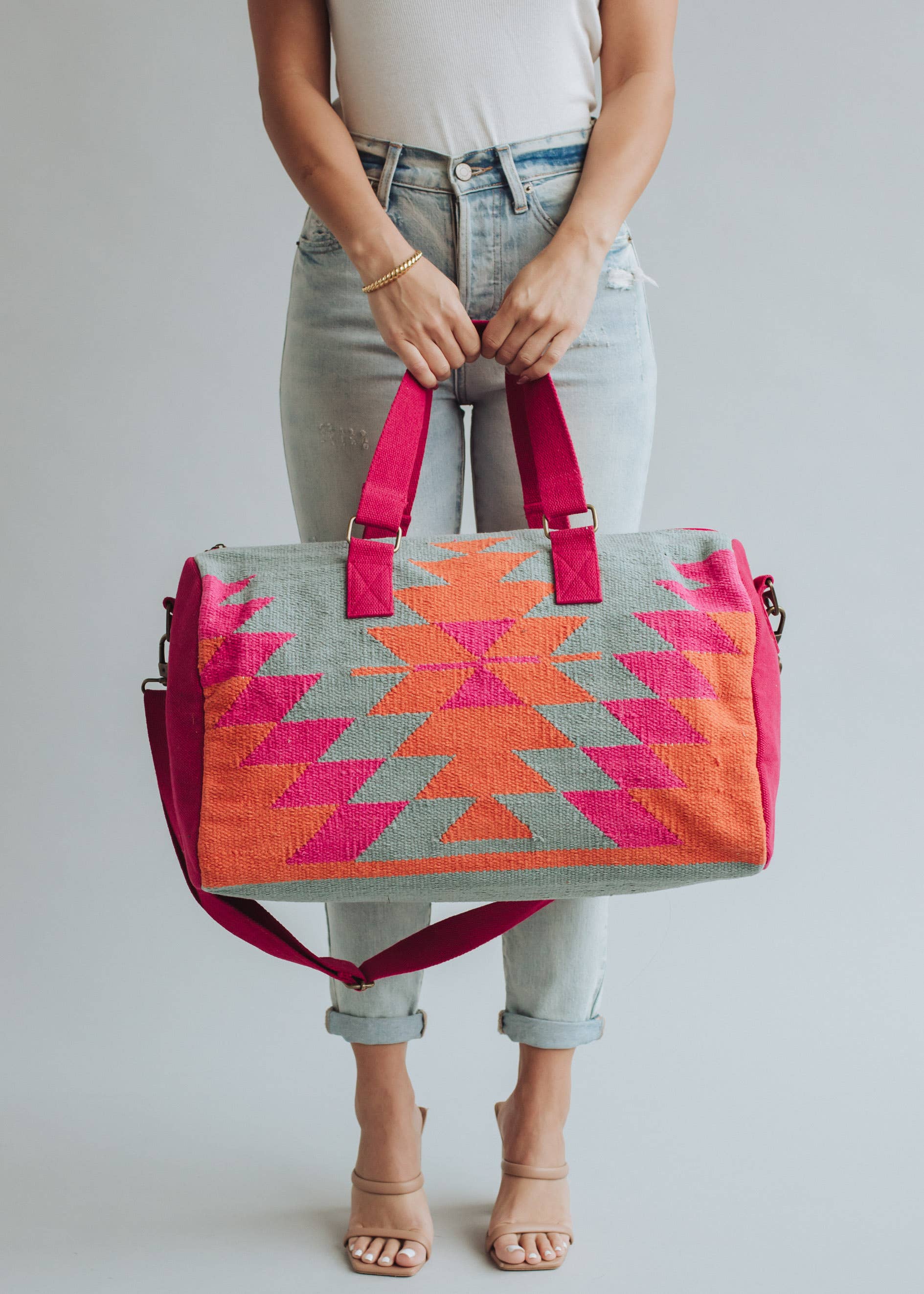 Vibrant weekender bag with orange and hot pink geometric design, held by woman in light wash jeans and white tank top