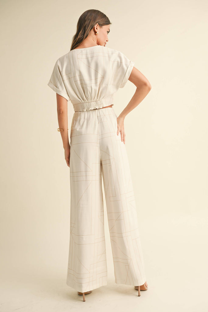 Woman wearing a cream two-piece set with geometric line print, knotted crop top, and wide-leg pants.