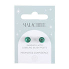 Hand holding a pair of malachite crystal stud earrings on a matching backing card with the text “Promotes Confidence.”
