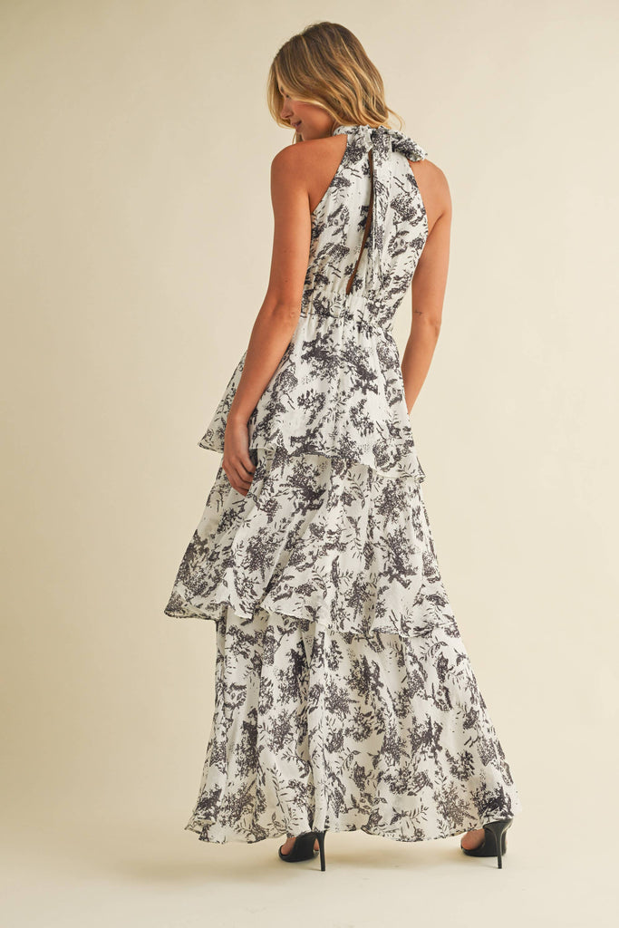 Woman wearing a halter neck tiered maxi dress with black floral print and ruffle layers
