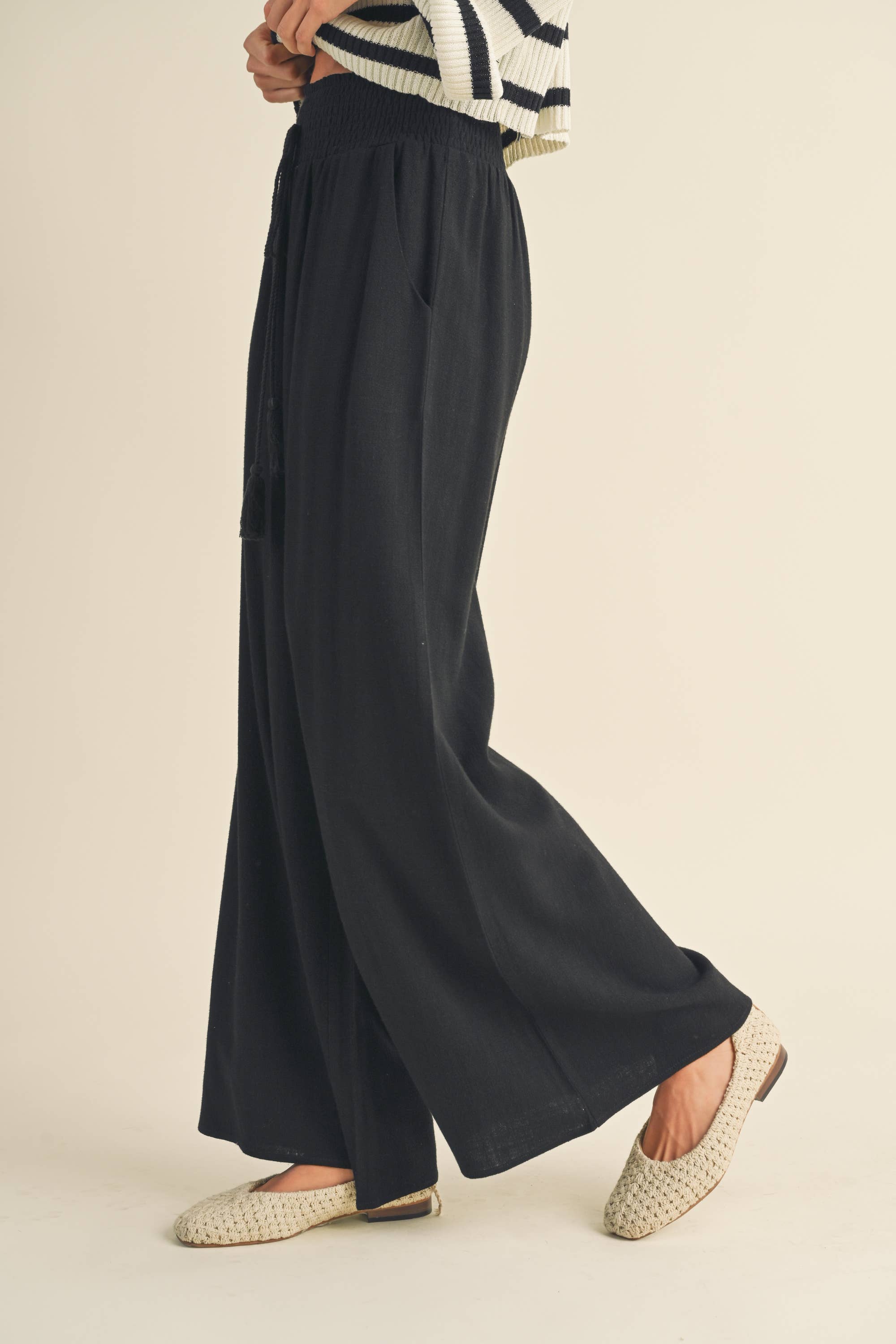 Woman wearing black wide-leg pants with smocked waistband and tassel drawstring.