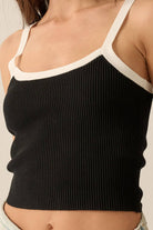 Black ribbed knit tank top with white trim on the straps and neckline, styled with light-wash denim jeans.