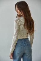Model wearing the Celestine Lace Top in cream and black lace with long sleeves and floral mesh pattern