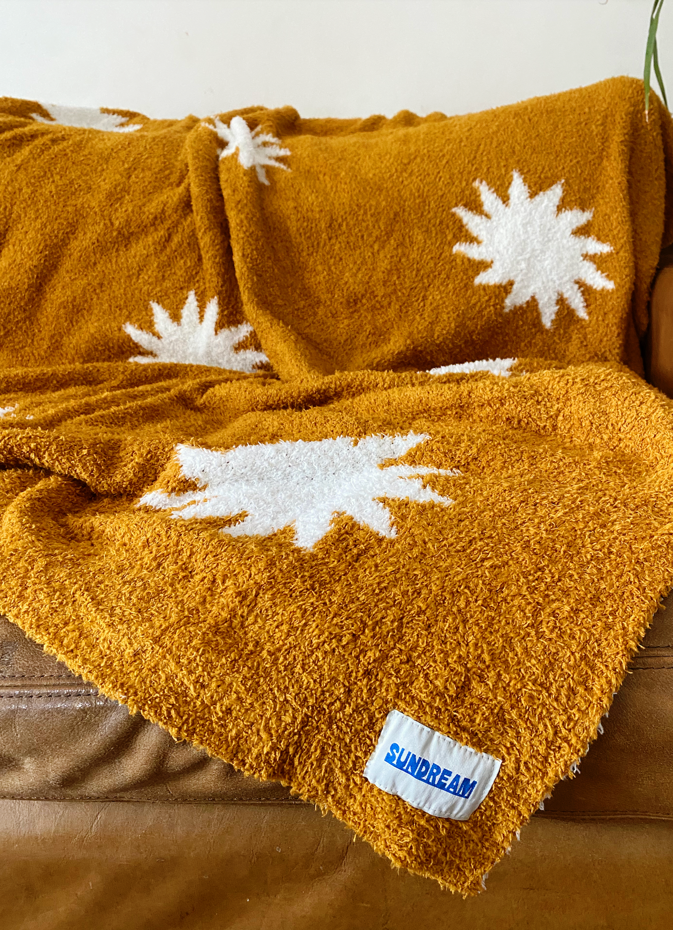 Cozy plush throw blanket in buckhorn brown with a white sunburst pattern, draped over a leather couch in a stylish and inviting living room.