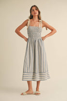 Woman wearing a blue and cream striped midi dress with smocked bodice and tie shoulder straps.