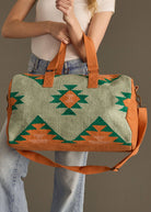 Sage green and rust weekender bag with geometric tribal pattern in green and orange, held by woman in jeans and white tank