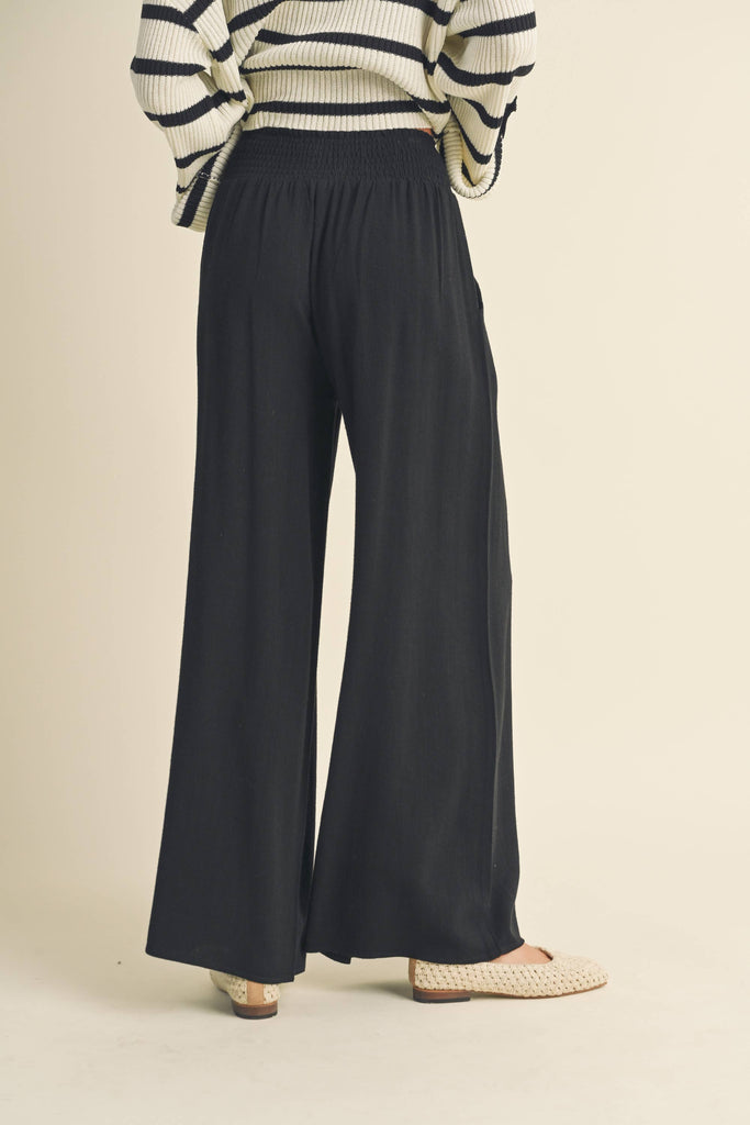 Woman wearing black wide-leg pants with smocked waistband and tassel drawstring.
