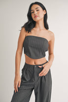 Woman wearing a strapless navy pinstriped crop top with tailored pleated pants.