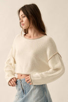 Woman wearing a sage green off-shoulder cropped sweater with white trim details and long sleeves.