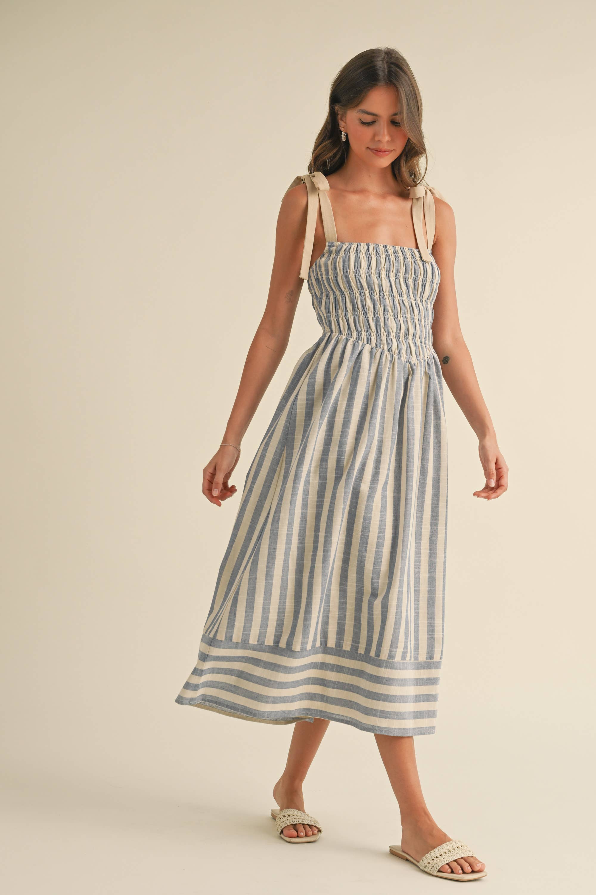 Woman wearing a blue and cream striped midi dress with smocked bodice and tie shoulder straps.