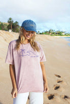Folded soft pink-colored t-shirt with a blue minimalist palm tree, wave, and "LIVE LOVE SURF" graphic.
