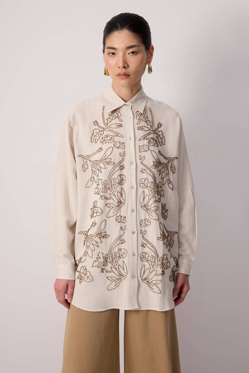 Model wearing a beige button-up shirt with floral embroidery and beaded detailing