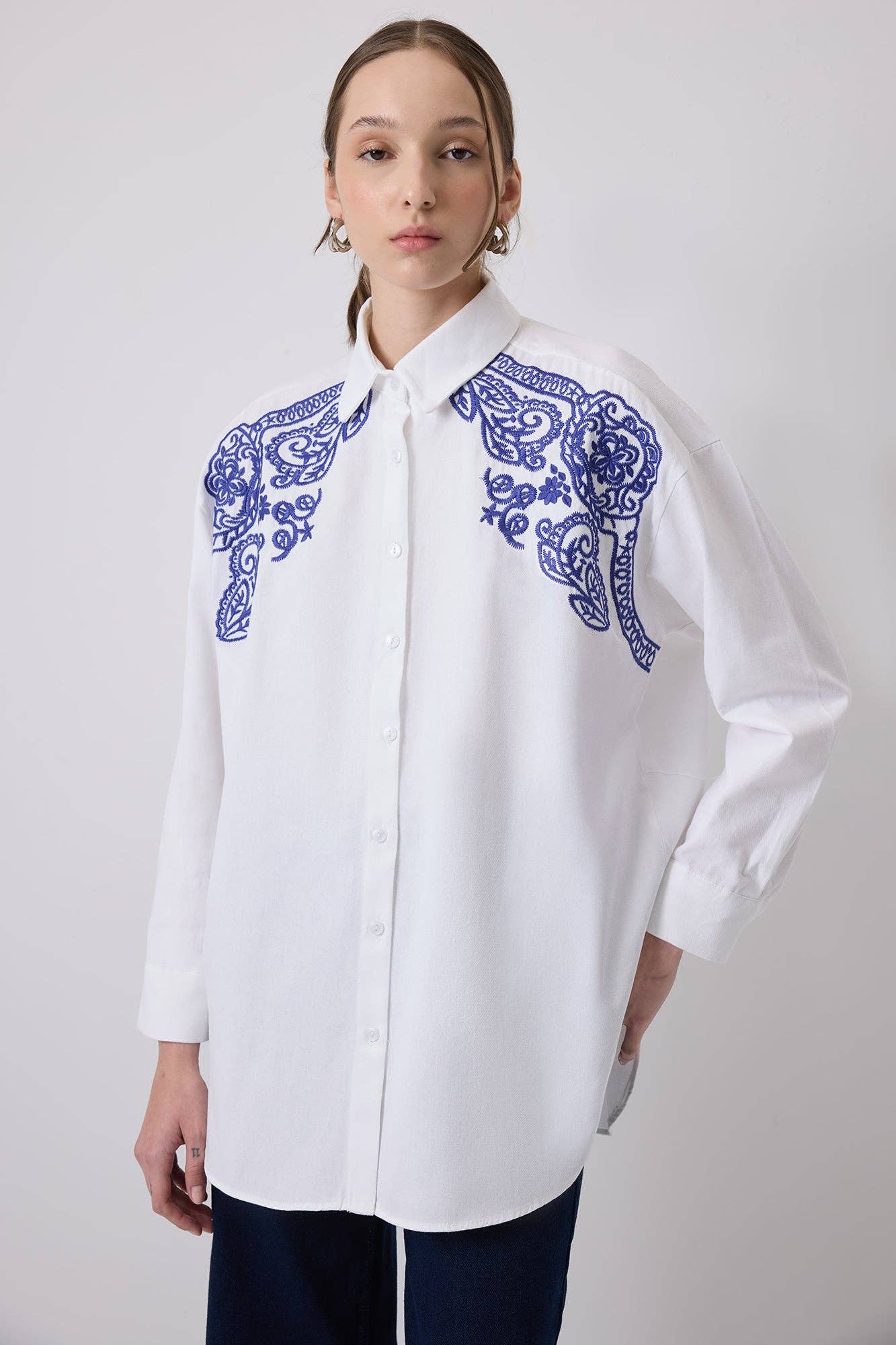 Woman wearing a white oversized shirt with bold blue embroidery on shoulders