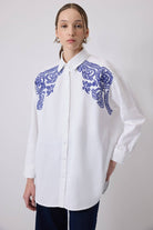 Woman wearing a white oversized shirt with bold blue embroidery on shoulders
