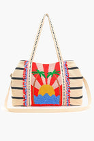 Beaded tote bag with sunset, palm tree, and ocean design, featuring black stripes, colorful pom-pom trim, and long handles.