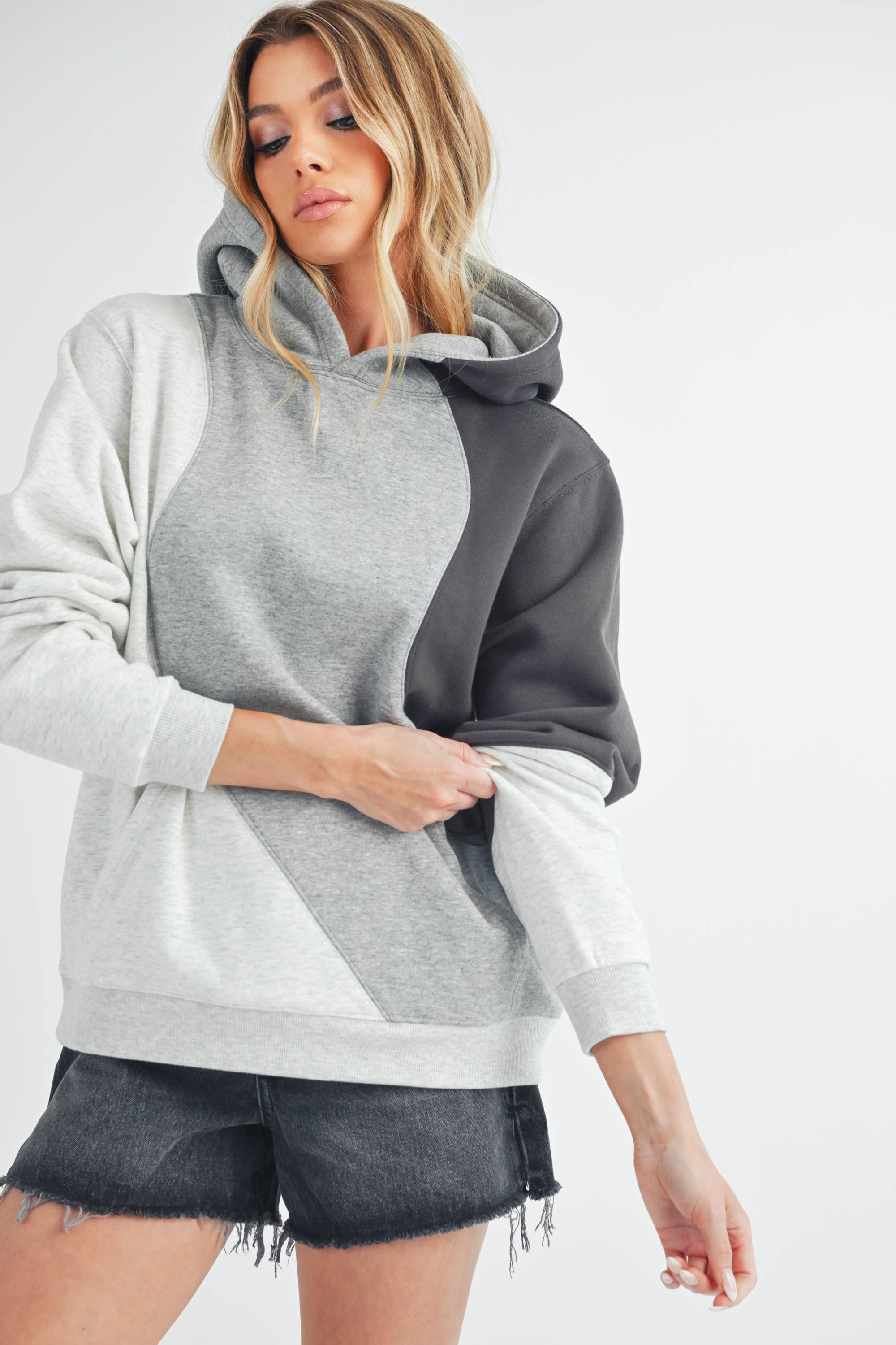 Woman wearing an oversized colorblock hoodie in grey, black, and ivory with a relaxed fit and kangaroo pocket.