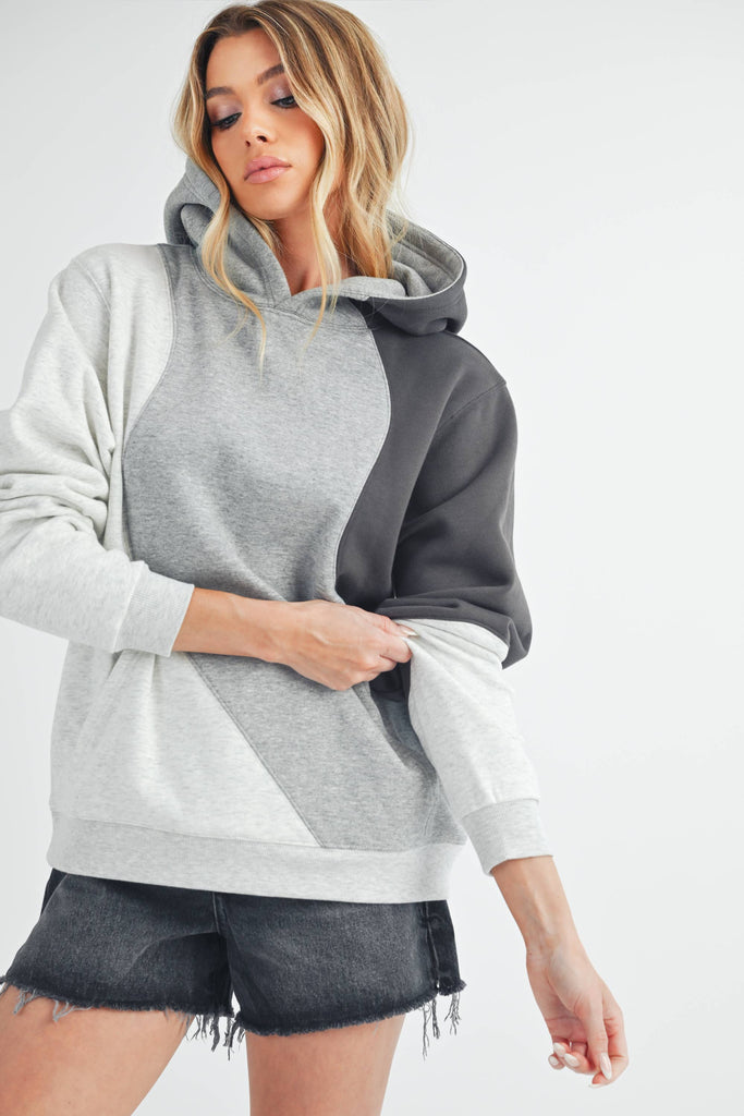 Woman wearing an oversized colorblock hoodie in grey, black, and ivory with a relaxed fit and kangaroo pocket.