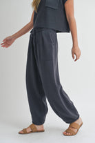 Woman wearing pleated bottom knitted pants in relaxed fit with drawstring waist and ankle detail.