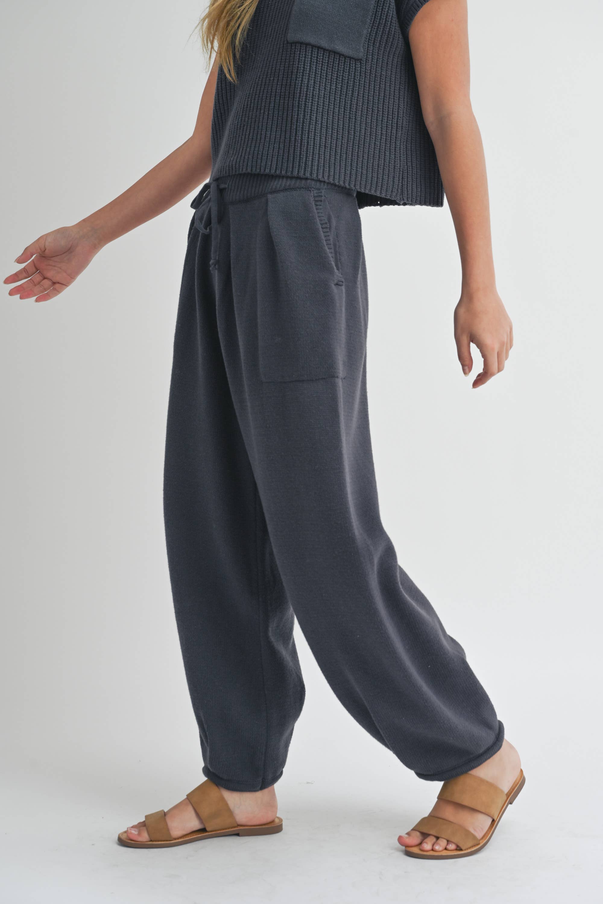 Woman wearing pleated bottom knitted pants in relaxed fit with drawstring waist and ankle detail.