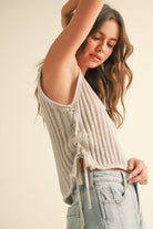 Woman wearing a ribbed knit top and light blue jeans against a beige background