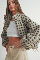 Woman wearing a beige and green checkered fleece jacket with a zip closure, paired with a white crop top and beige corduroy pants.