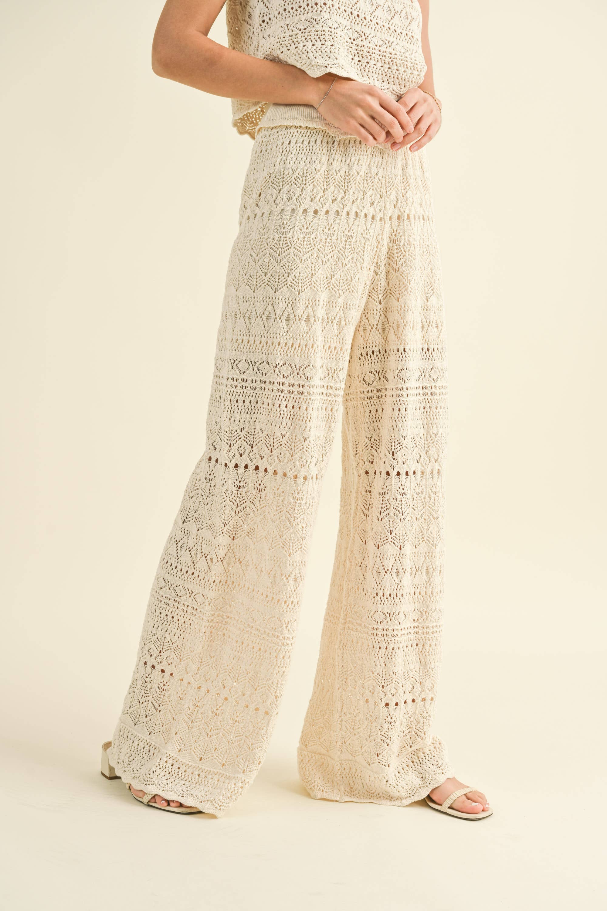 Model wearing cream-colored crochet wide-leg pants with intricate patterns and a high waist.