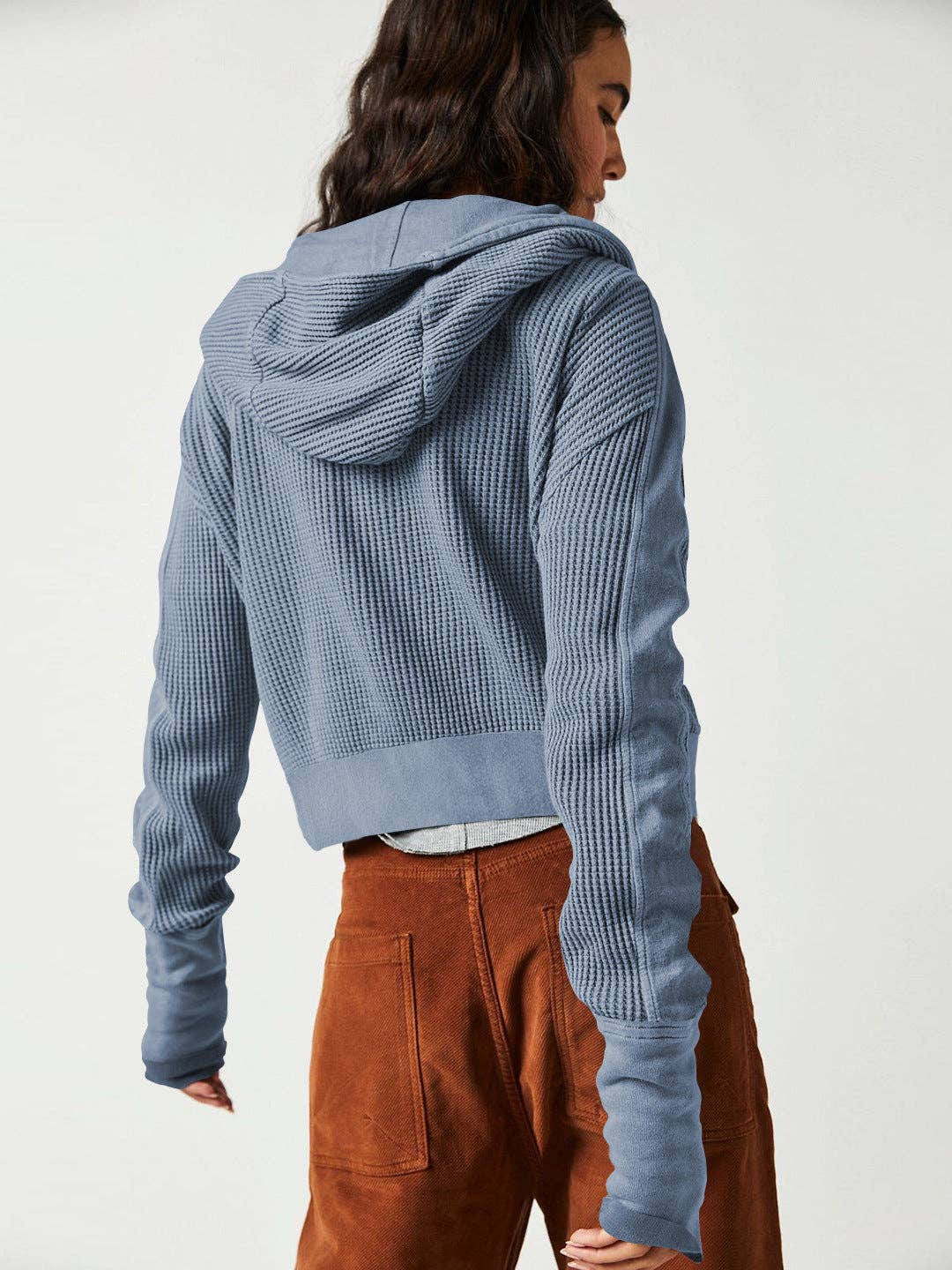 Woman wearing a Sahara Sky Hooded Jacket with a zip-up front, textured waffle knit, and button detailing in blue and brown tones.
