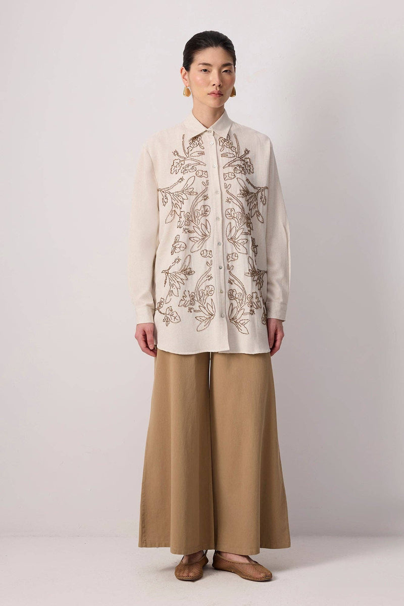 Model wearing a beige button-up shirt with floral embroidery and beaded detailing