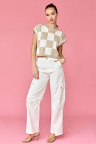 Woman wearing a taupe and white loose-fit checker knit top with white pants.