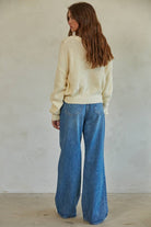 Woman wearing a cream chunky knit pullover sweater with relaxed fit, styled casually with light-wash jeans.